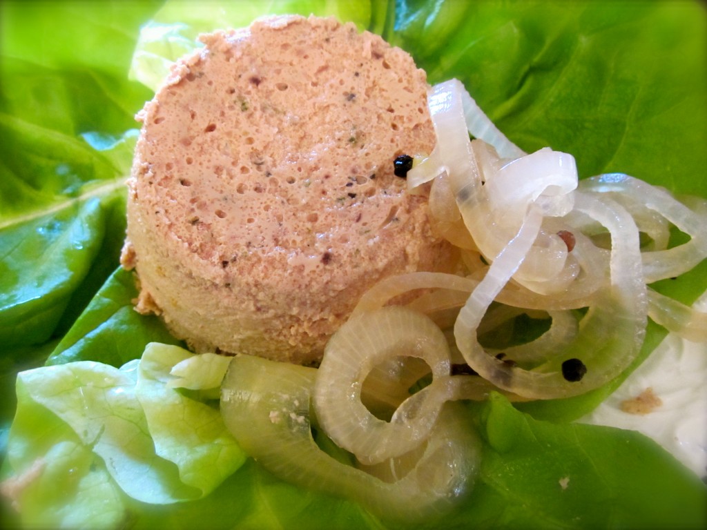 An unmolded chicken liver gâteaux served on a bed of butter lettuce tossed with champagne vinaigrette and pickled onions.